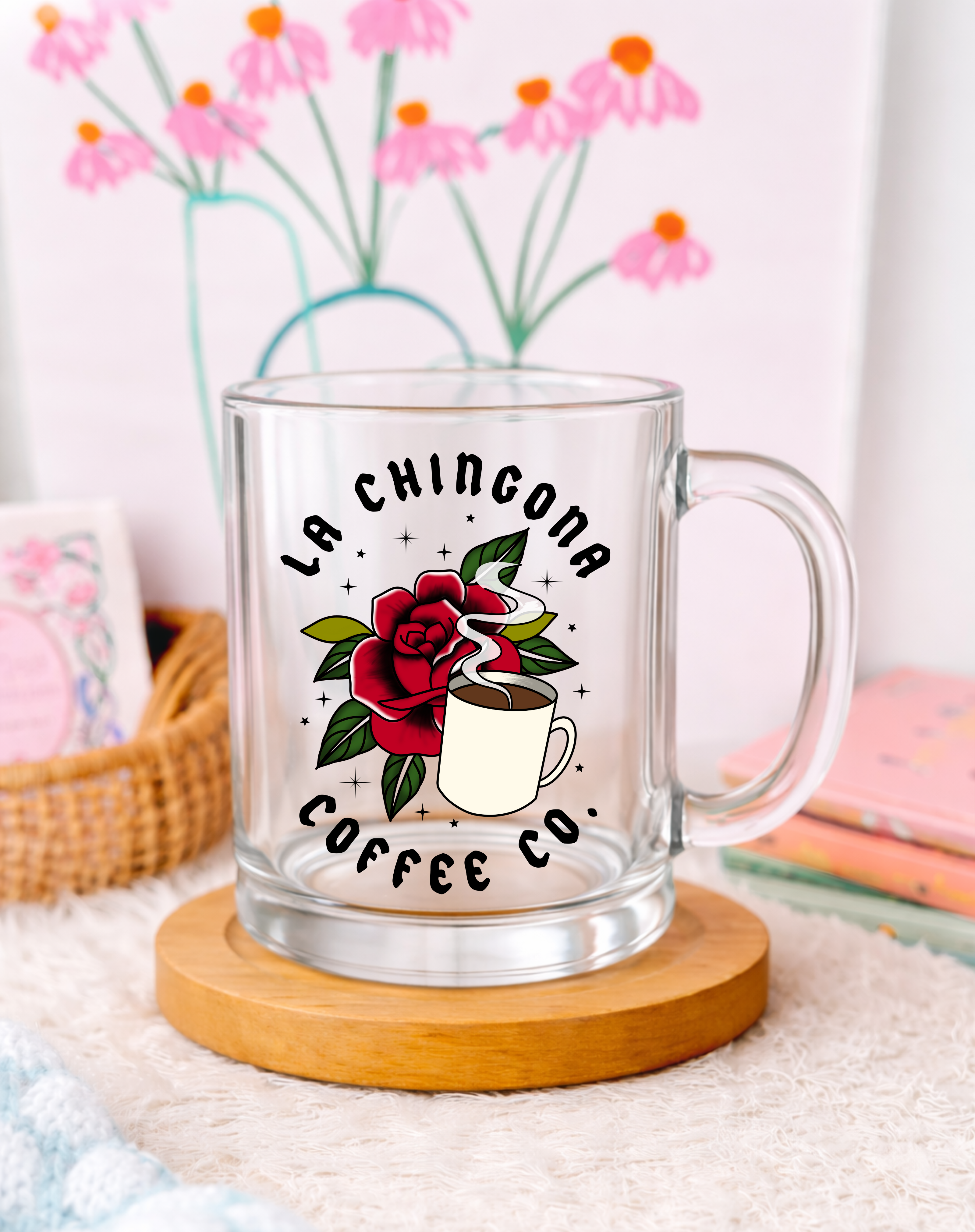 Clear glass mug with 'La Chingona Coffee Co' design on a wooden coaster with flowers in the background