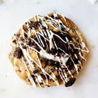 Cookie with Oreo pieces and white chocolate drizzle on a marble surface