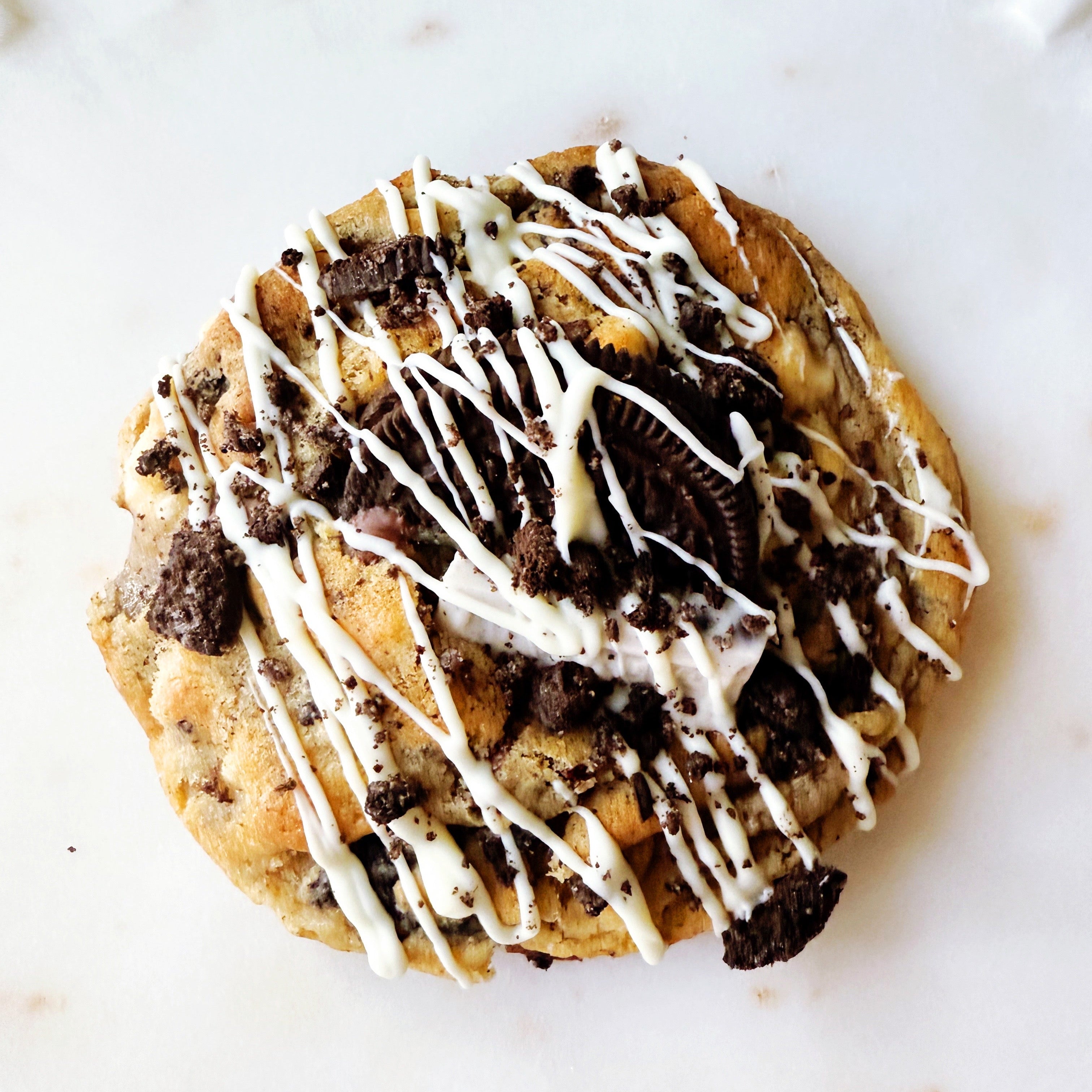 Cookie with Oreo pieces and white chocolate drizzle on a marble surface