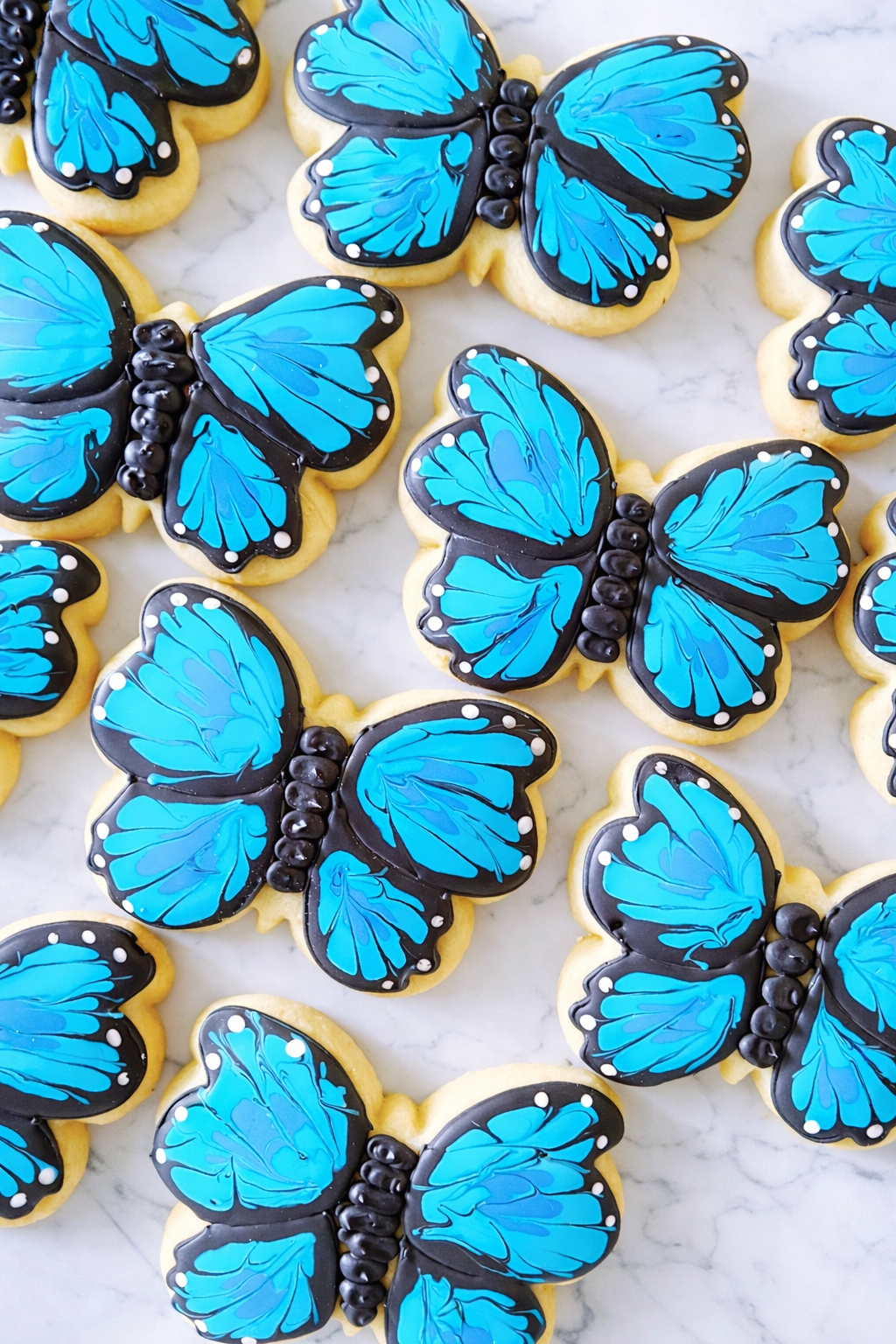 Decorated butterfly sugar cookies with bright blue and black icing and white detailing on a marble background.